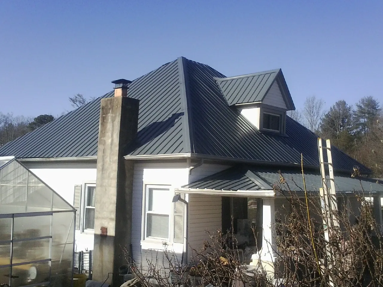 Dark blue standing seam metal roof on a white farmhouse with dormer — Slate & Tile Roof Repair by Roofing Brothers in De Witt