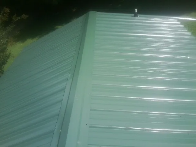 New green metal panels meeting at the ridge of a roof — Flat Roof Repair work by our crew in De Witt