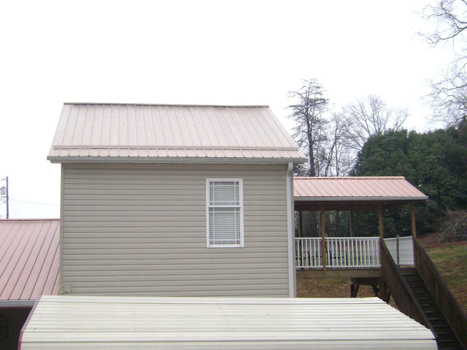 Tan metal roofs on a two story addition and attached porch, from a Roof Replacement job in De Witt